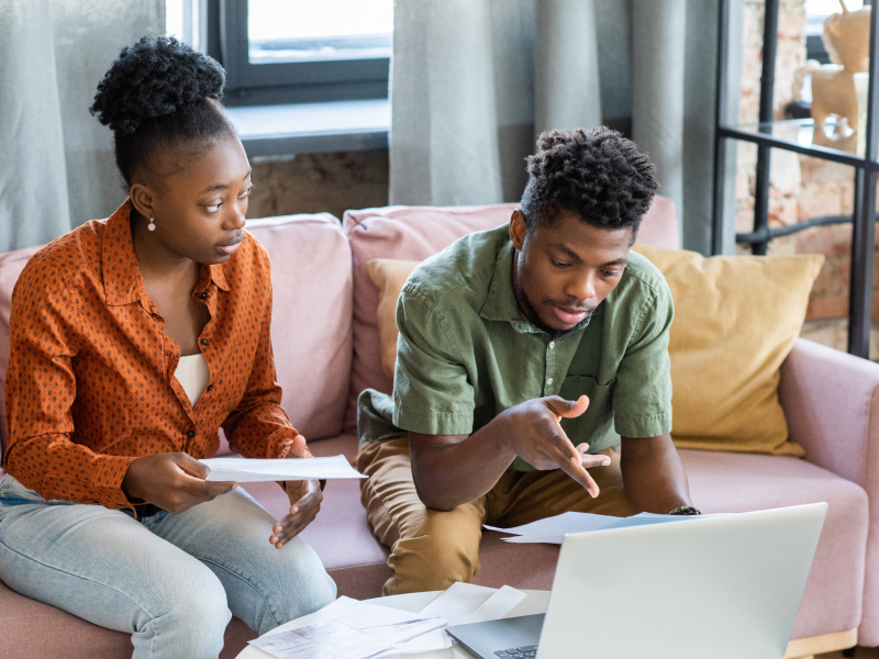 A couple looks frustrated as they look at bills and a laptop screen